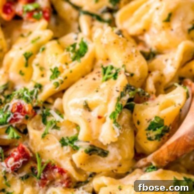 Close up photo of a wooden spoon in a pot of tortellini alla panna.