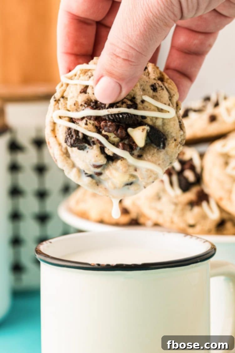 A woman's hand dipping a freshly baked Chocolate Chip Oreo Cookie into a mug of milk, highlighting its soft texture.