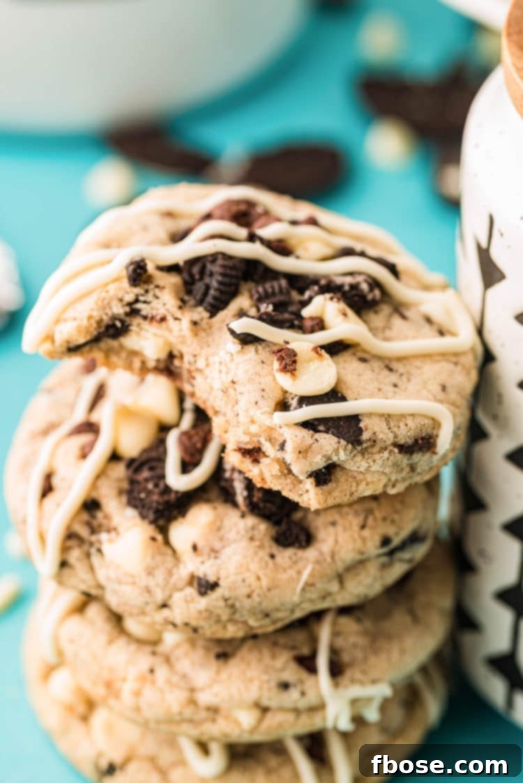 A stack of oreo chocolate chip cookies leaning against a mug with the top one missing a bite, tempting the viewer.