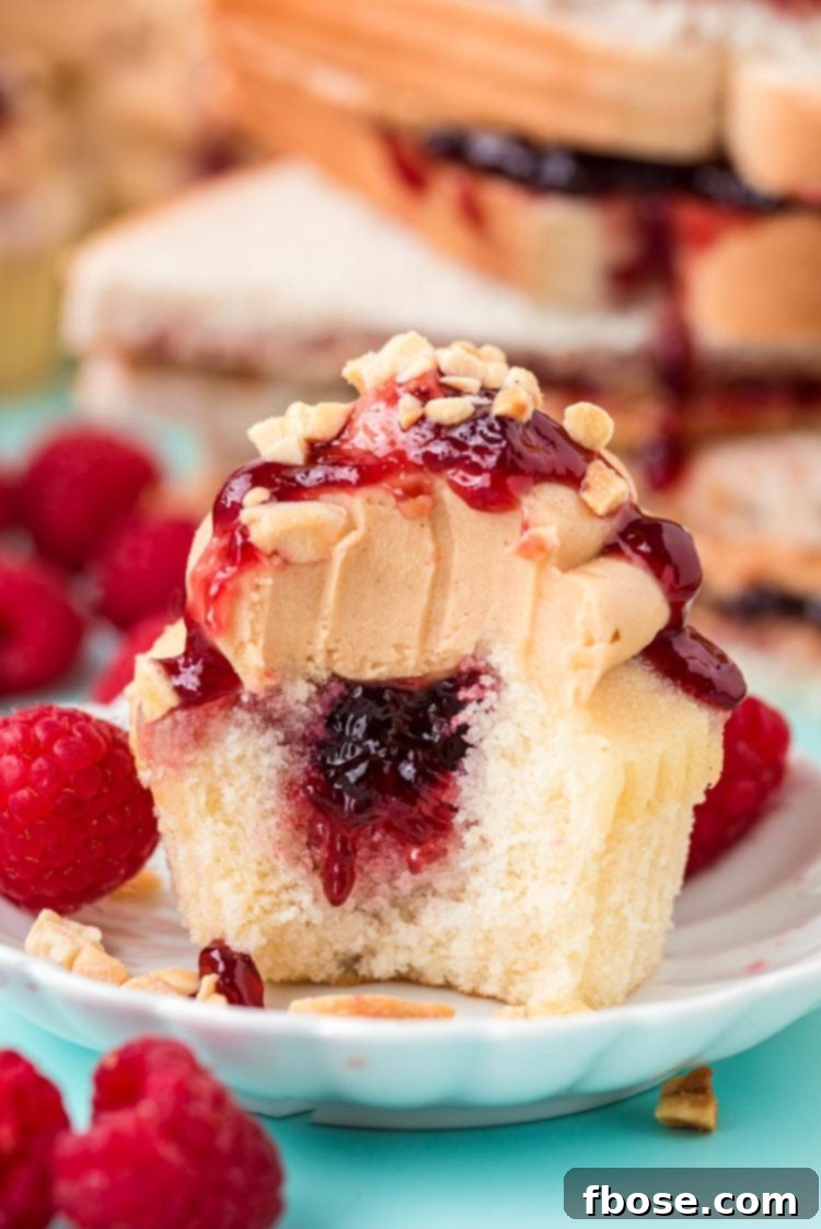A peanut butter and jelly cupcake with a bite taken out of it, revealing the bright red raspberry filling at its core.