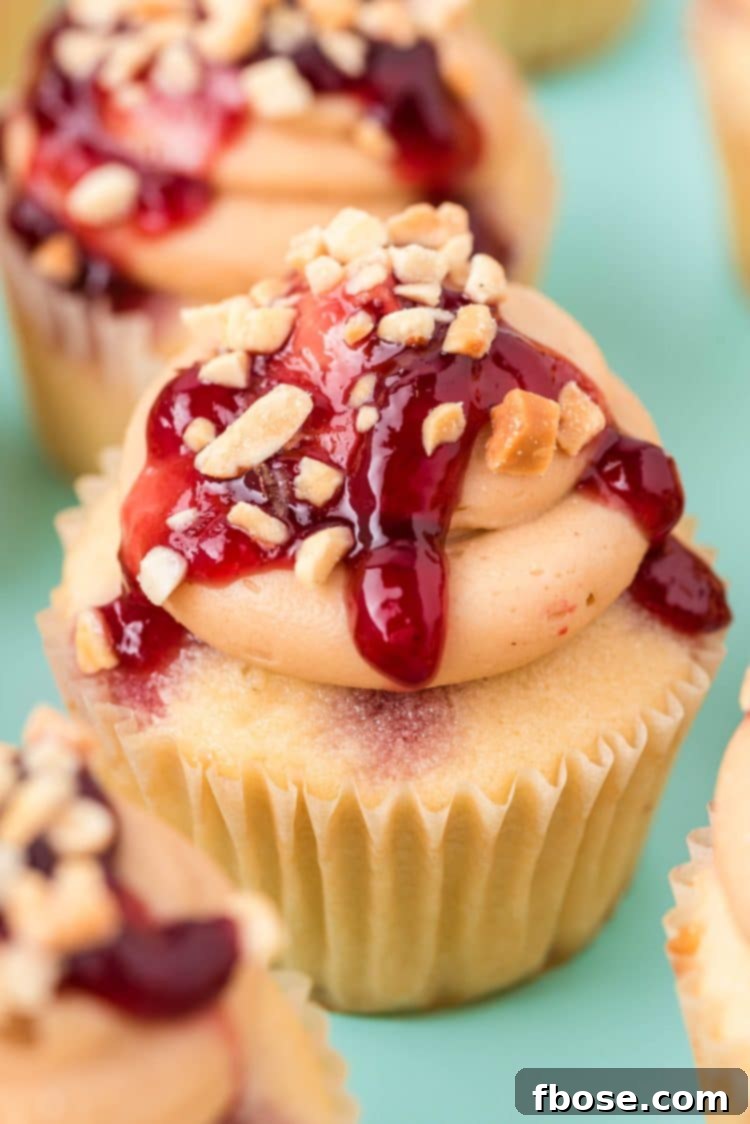 A single peanut butter jelly cupcake on a blue surface, surrounded by other frosted cupcakes, ready to be enjoyed.