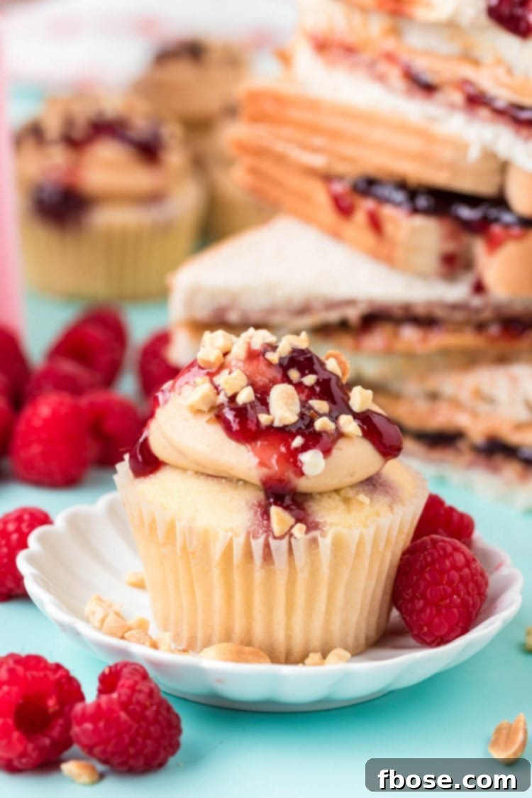 A single beautifully frosted peanut butter and jelly cupcake on a white plate, placed on a textured blue surface.