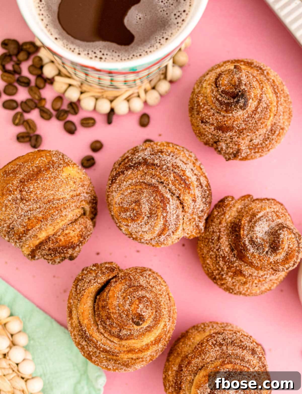 Overhead photo of cruffins on a pink surface with a mug of coffee.