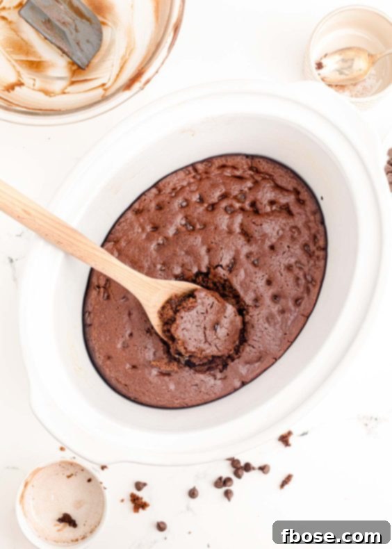 Ultimate Homemade Crockpot Chocolate Cake 15 A wooden spoon scooping chocolate cake out of a white crockpot.