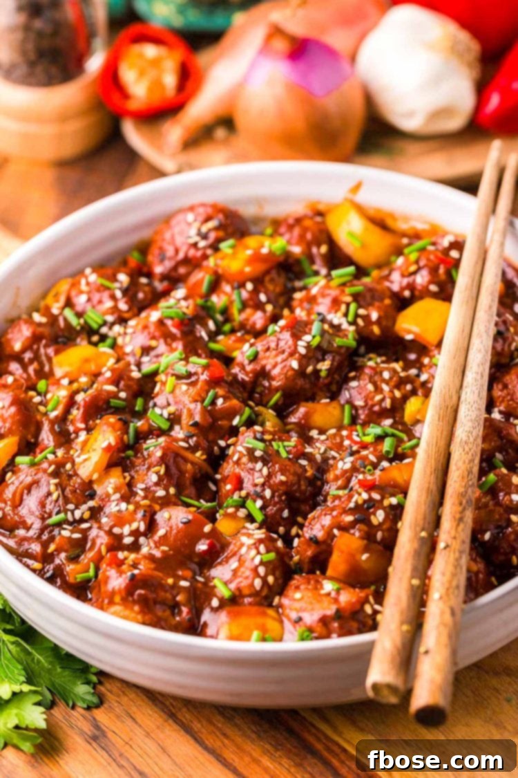 Close up of chicken manchurian in white bowl on a wooden table with chopsticks resting together on top of the bowl.