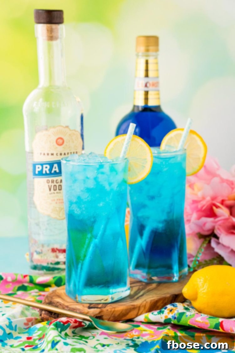 Two glasses filled with bright blue Sex in the Driveway cocktails, garnished with lemon slices.