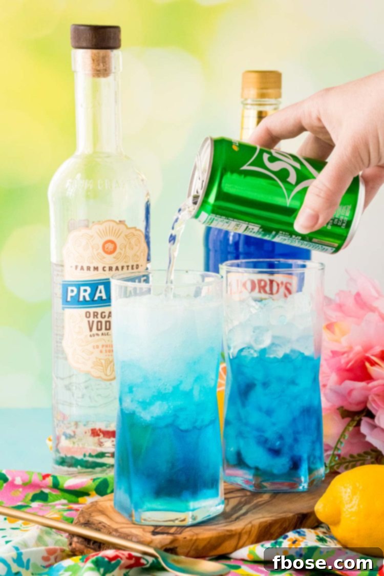 Lemon-lime soda being poured into a blue Sex in the Driveway cocktail glass, creating a fizzy top.