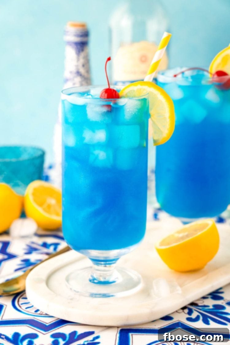 Azure Escape 3 Two exquisite Blue Lagoon cocktails presented in stemmed highball glasses on a pristine white marble tray, exuding a luxurious and refreshing appeal.