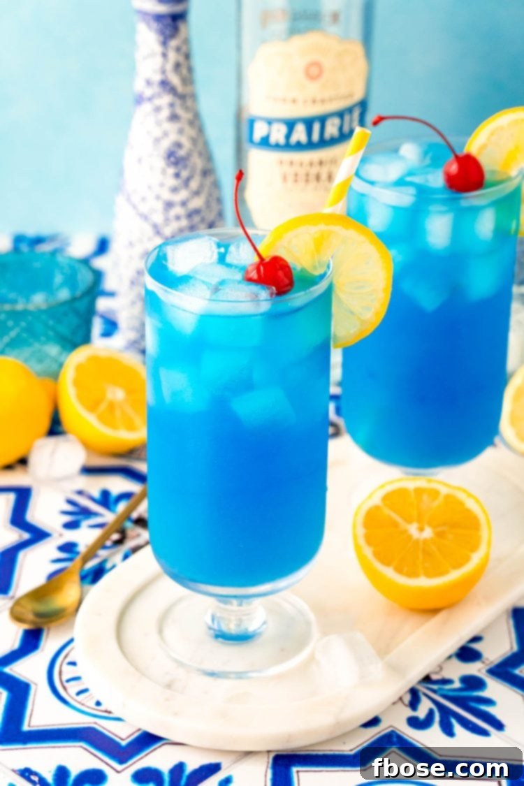 Azure Escape 6 Two visually striking Blue Lagoon cocktails, each perfectly prepared and served in elegant stemmed highball glasses, arranged on a pristine white marble tray.