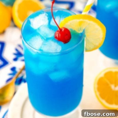 Blue Lagoon cocktail garnished with lemon and a maraschino cherry on a white marble tray.