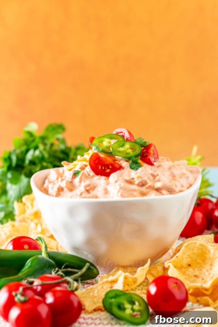 Boat dip (taco dip) in a white bowl surrounded by fresh produce.