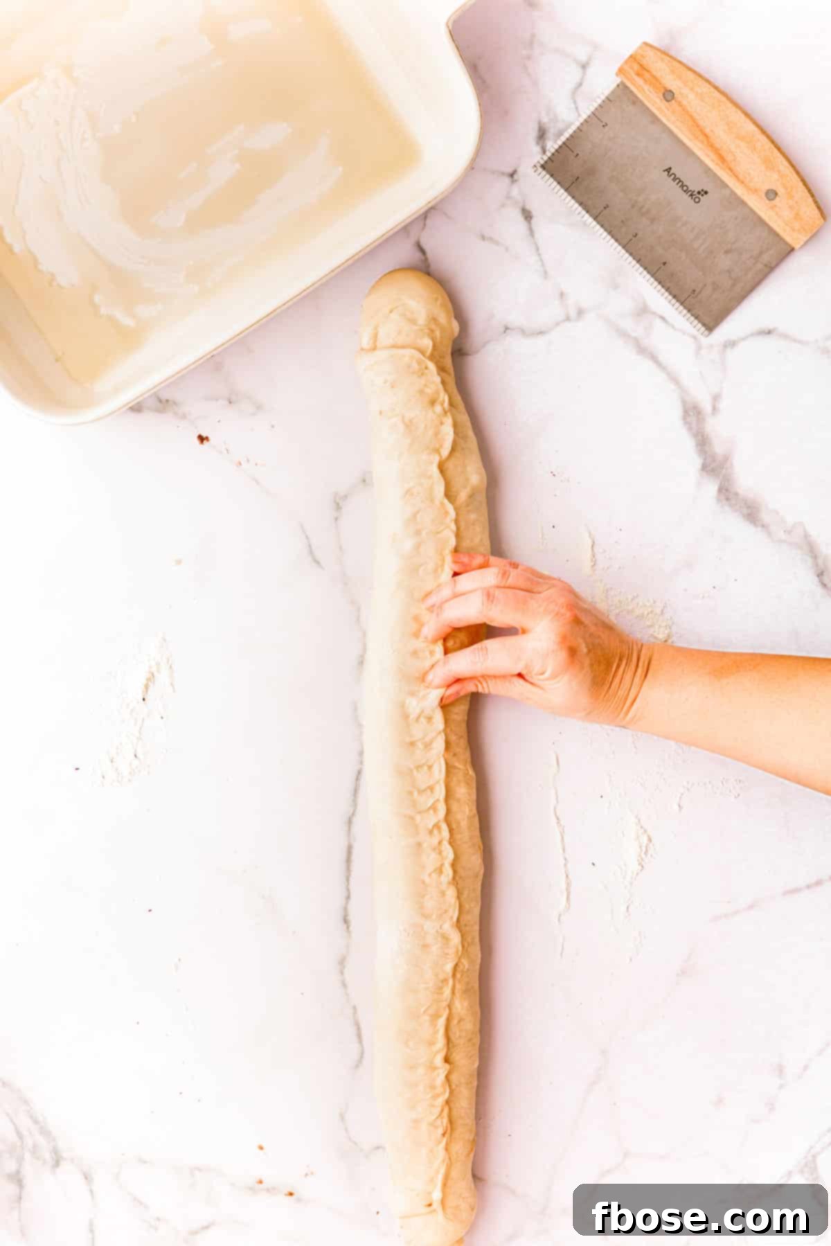 Decadent Chocolate Cinnamon Swirls 12 A woman's hand pinch the seams of dough on a log of cinnamon rolls.