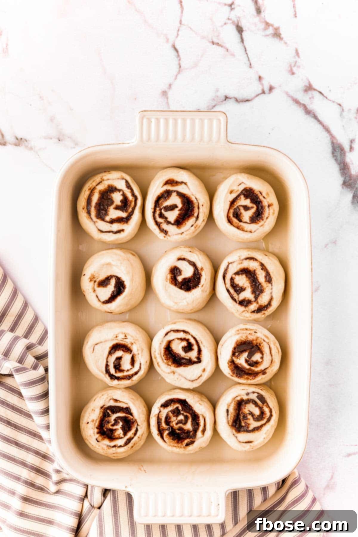 Decadent Chocolate Cinnamon Swirls 13 Cinnamon rolls that have been sliced in a baking dish to rise.