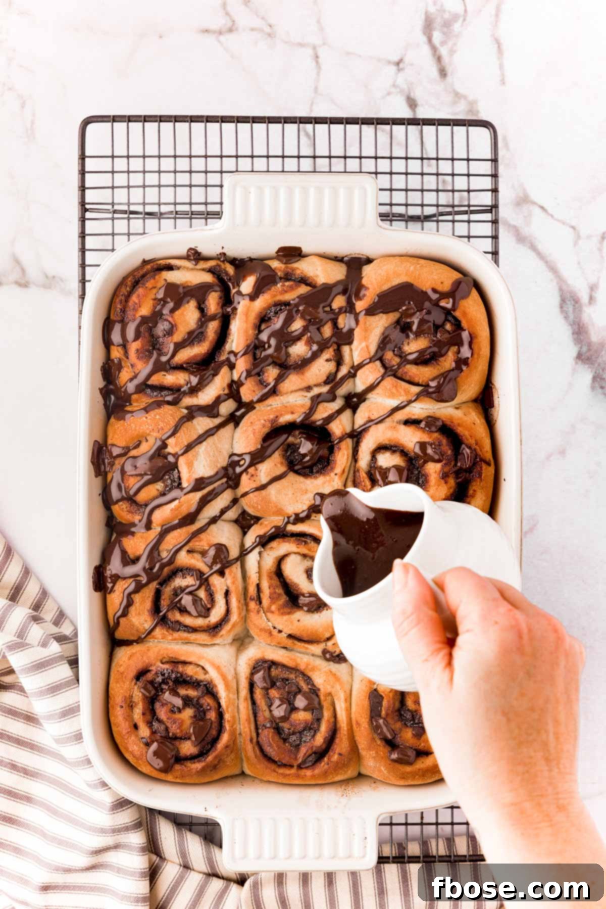 Decadent Chocolate Cinnamon Swirls 16 Chocolate glaze being poured over a freshly baking batch of chocolate cinnamon rolls.