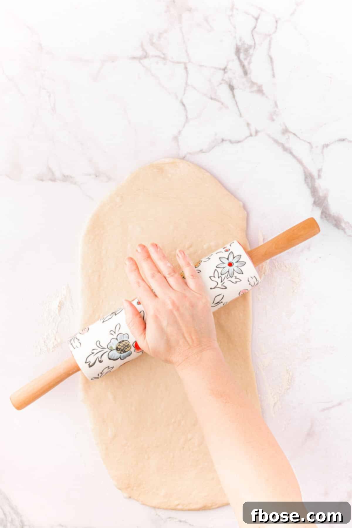 Decadent Chocolate Cinnamon Swirls 10 A woman's hand using a rolling pin to shape dough for cinnamon rolls.