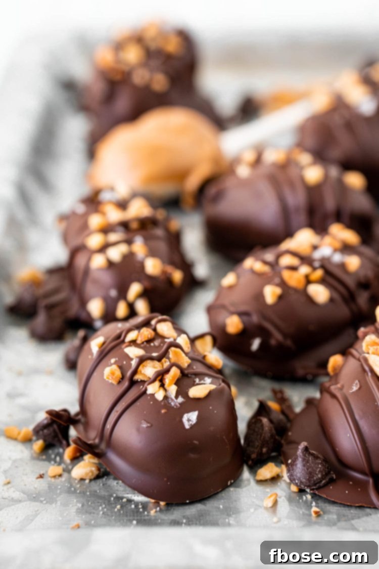 Close-up photo of chocolate-covered Snickers stuffed dates, garnished with chopped peanuts and flaky sea salt.