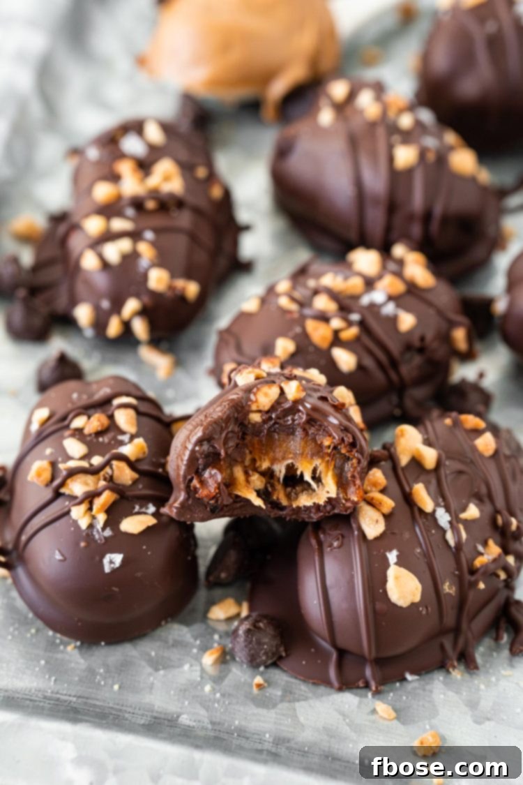 A close-up of Snickers stuffed dates on a metal serving tray, one date shows a bite taken out, revealing the peanut butter and peanut filling.