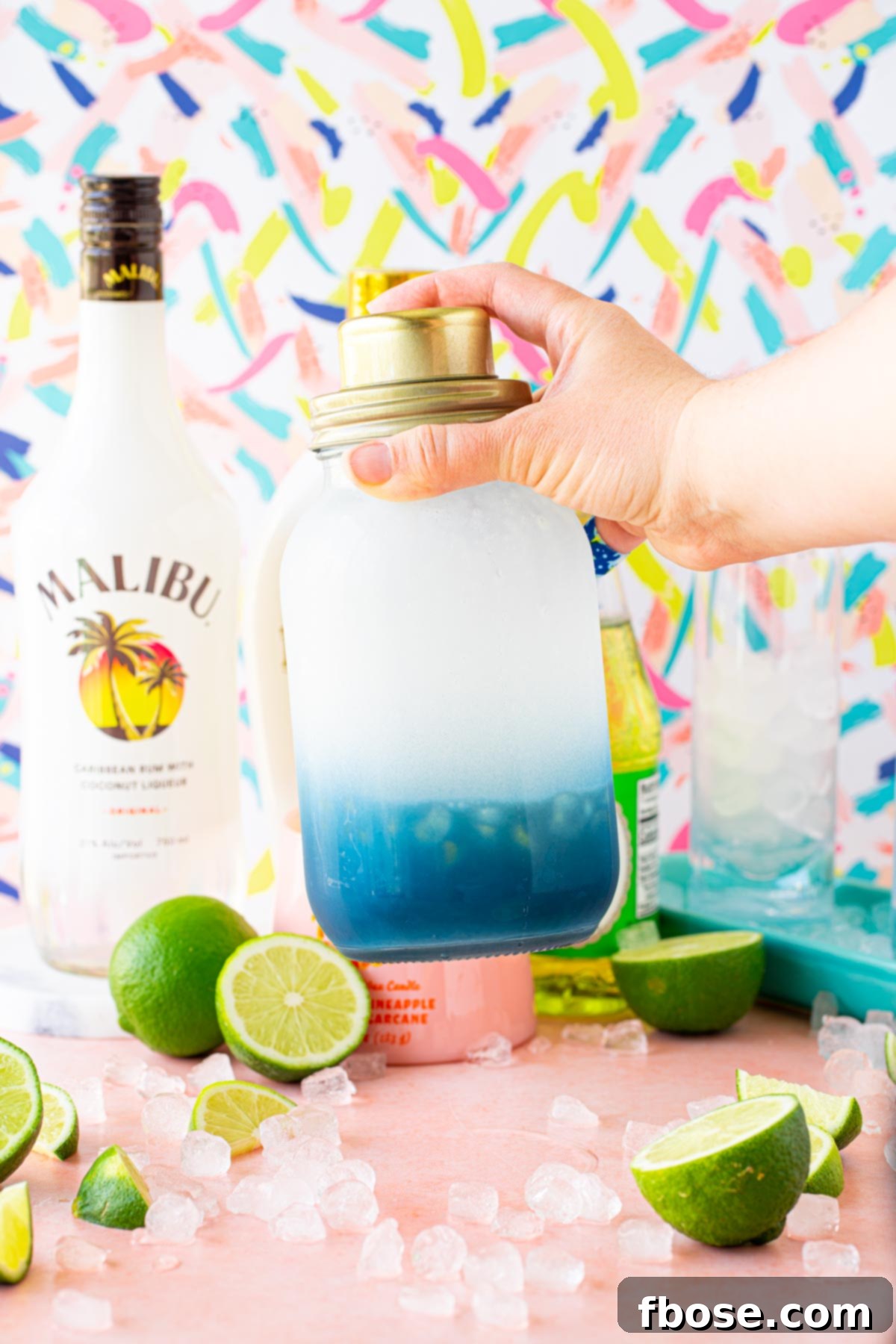A cocktail being shaking in a vibrant blue and clear cocktail shaker.