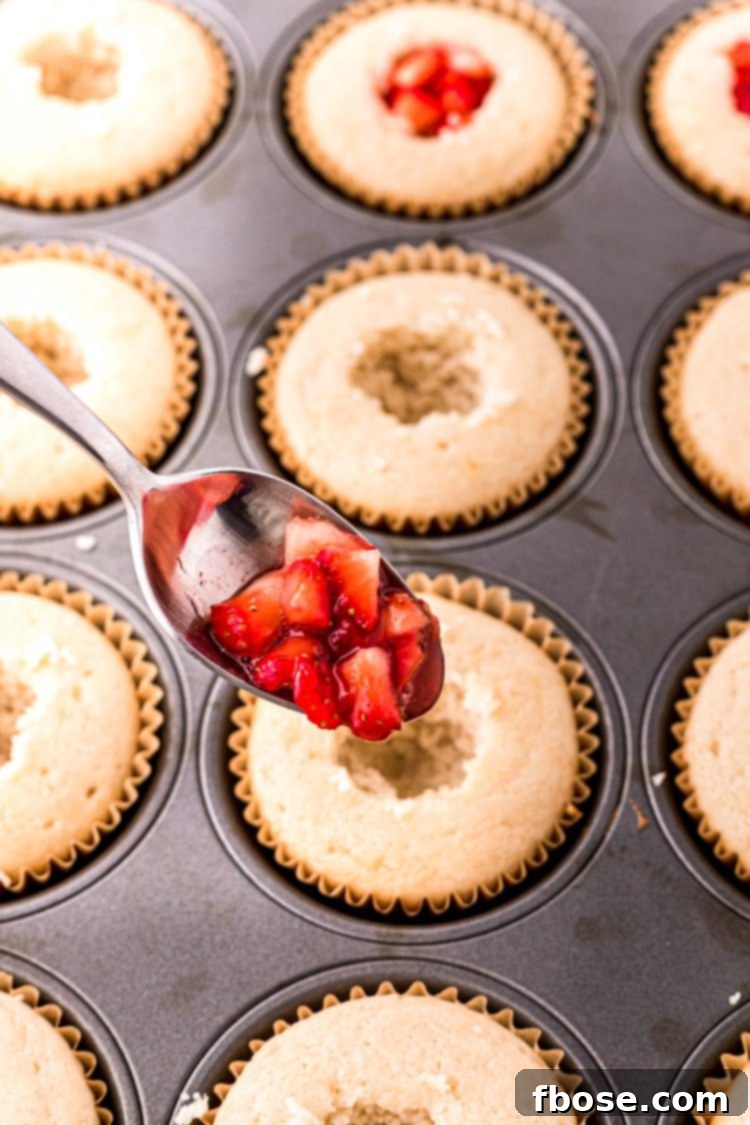 Strawberry filling being added to cored out vanilla cupcakes.