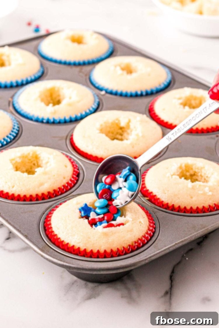 Red, white, and blue sprinkles being added to vanilla cupcakes.