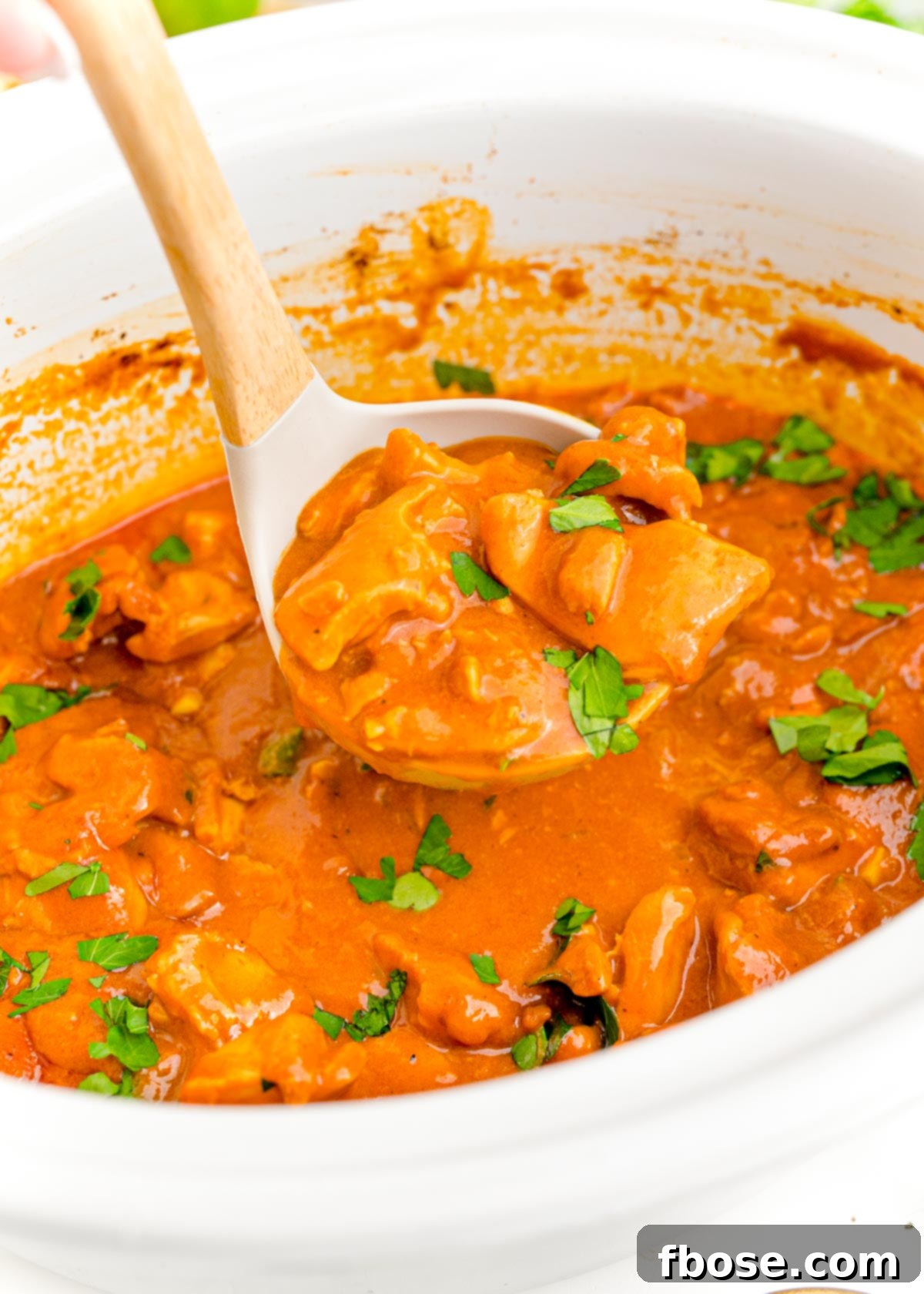 A ladle gracefully scooping creamy slow cooker butter chicken from a pristine white crockpot, highlighting its rich texture.