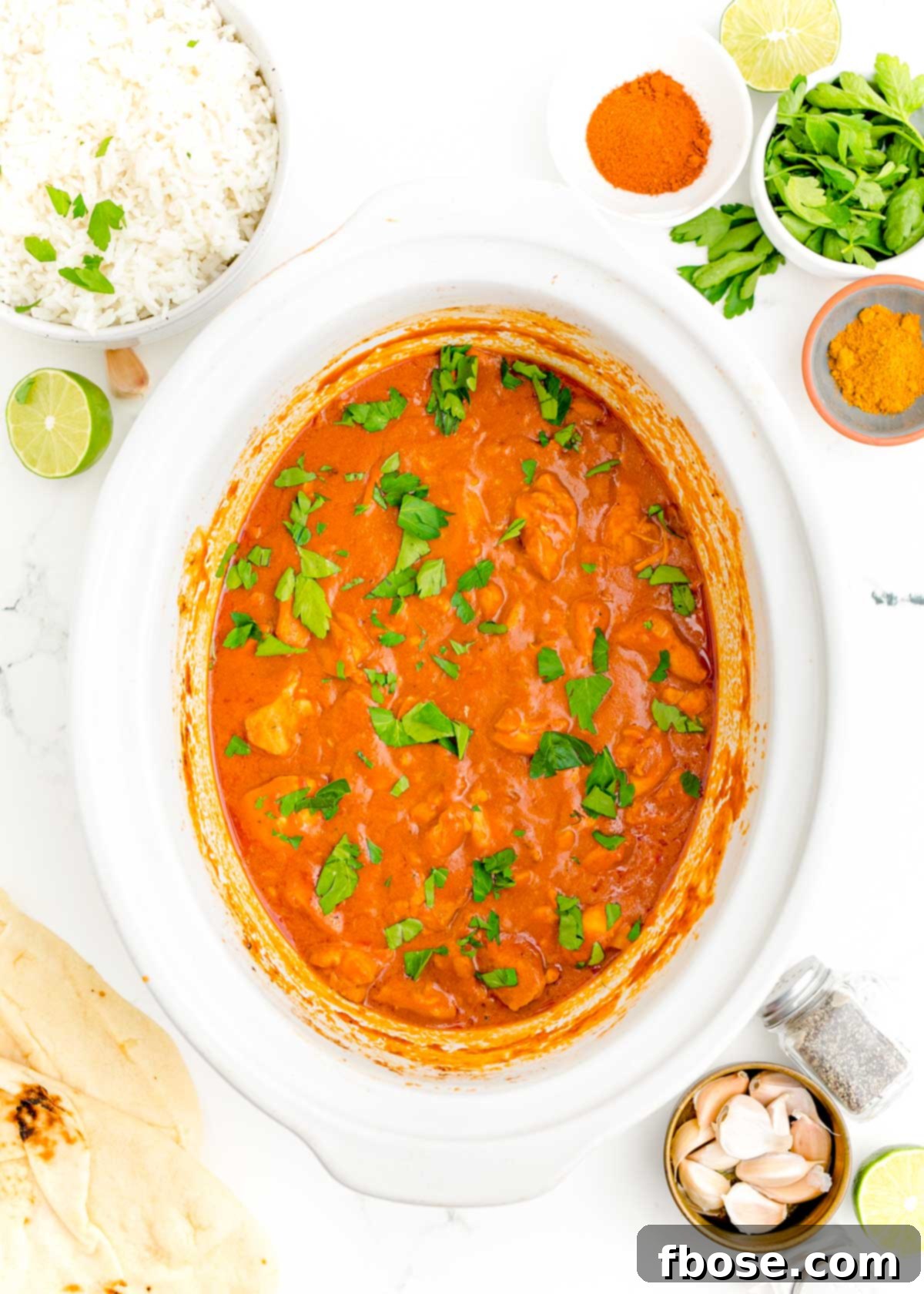 Overhead shot of a white crockpot brimming with delicious slow cooker butter chicken, ready to be served.