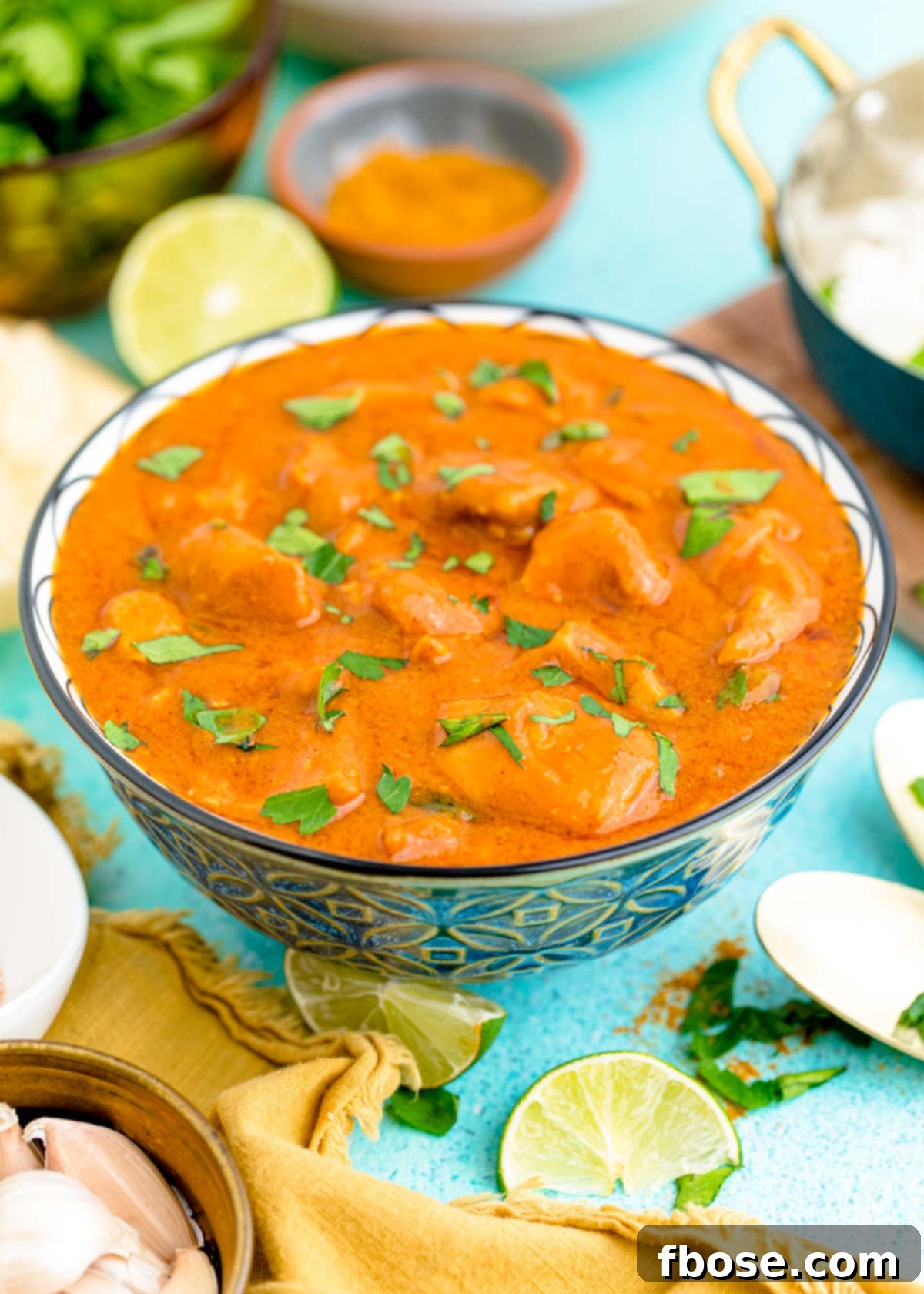 Close-up of Slow Cooker Butter Chicken in a vibrant blue bowl, garnished with fresh cilantro, resting on a teal textured surface.