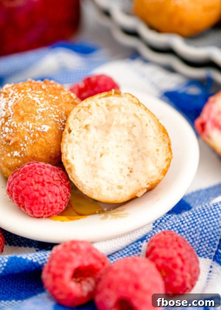 A fried cheesecake bite cut open on a white plate with raspberries around it.