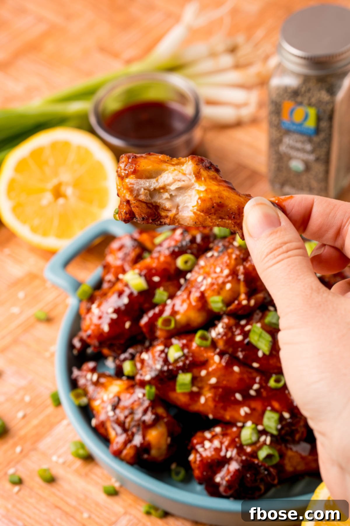 Sticky Korean BBQ Chicken Wings 9 A woman's hand holding up a chicken wing with a bite missing.