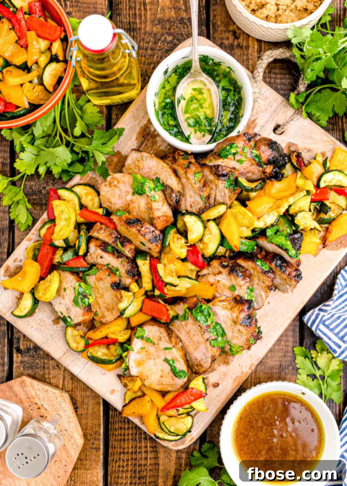 Succulent Grilled Pork Tenderloin 2 Overhead photo of pork tenderloin sliced on a wooden cutting board with vegetables.