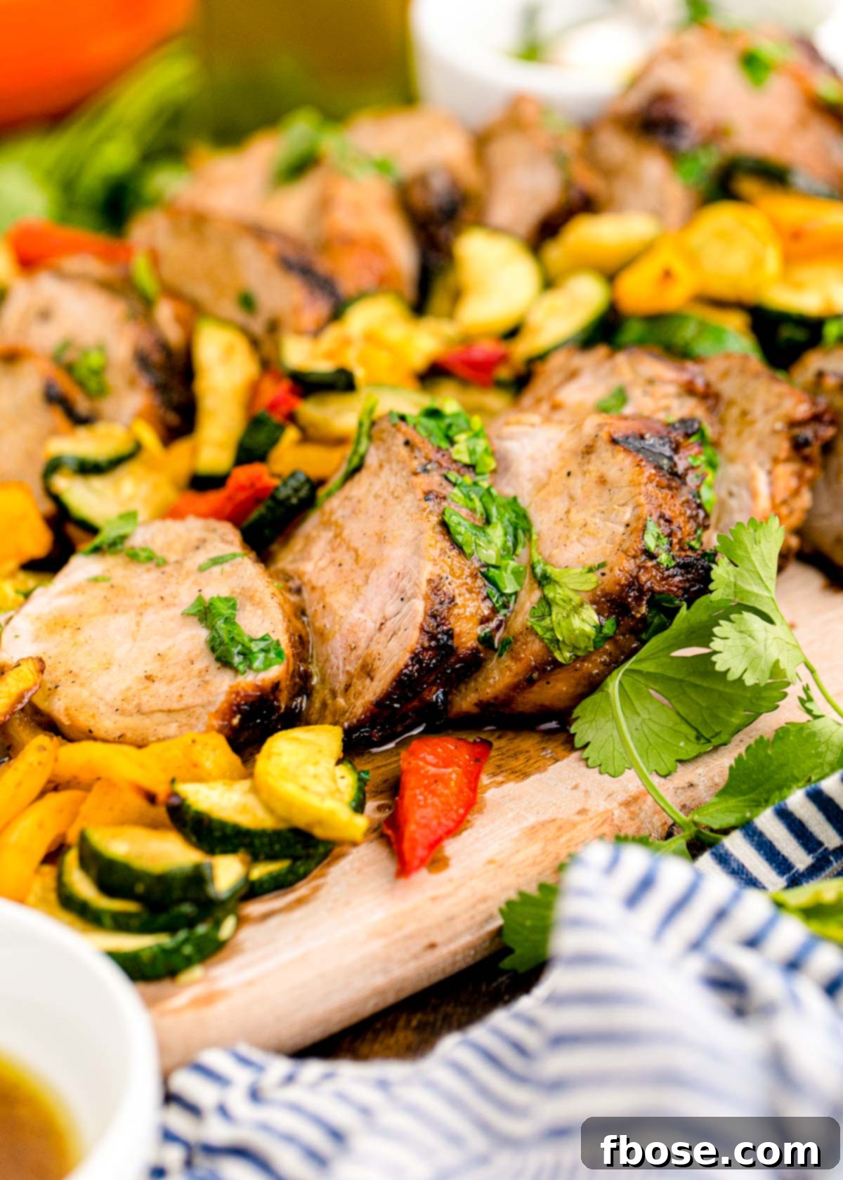 Succulent Grilled Pork Tenderloin 3 Pork tenderloin on a wooden cutting board sliced up.