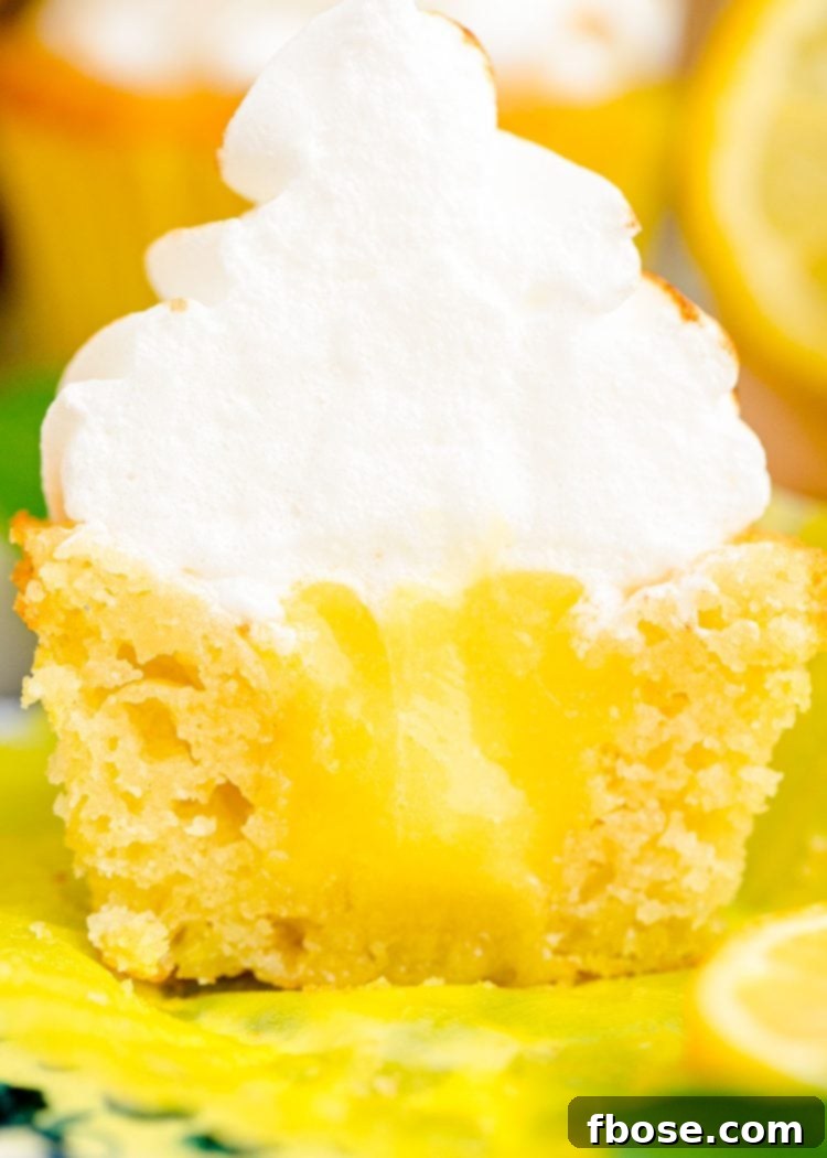 A lemon meringue cupcake cut in half to reveal lemon curd inside.