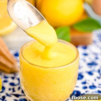 A spoon scooping lemon curd out of a glass dish.