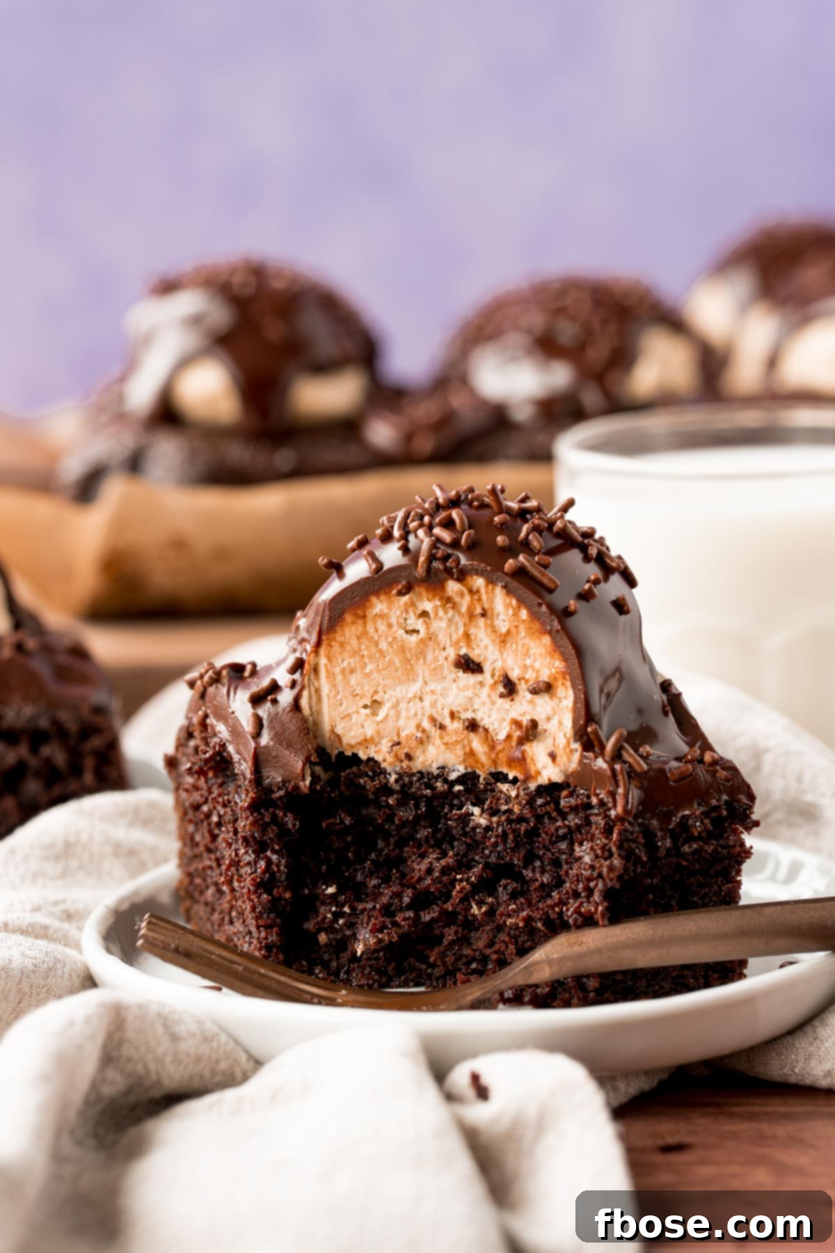 Close up photo of a slice of chocolate cake topped with a scoop of peanut butter frosting and topped with ganache.