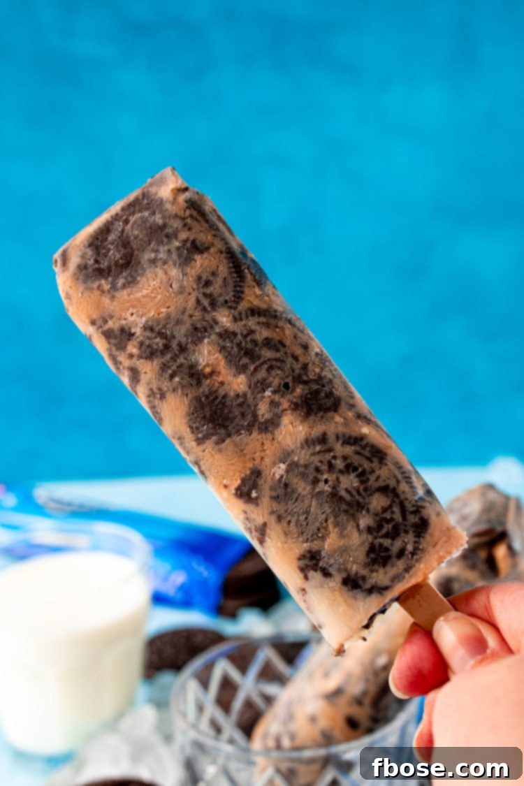 A woman's hand holding a cookies and cream popsicle to the camera.