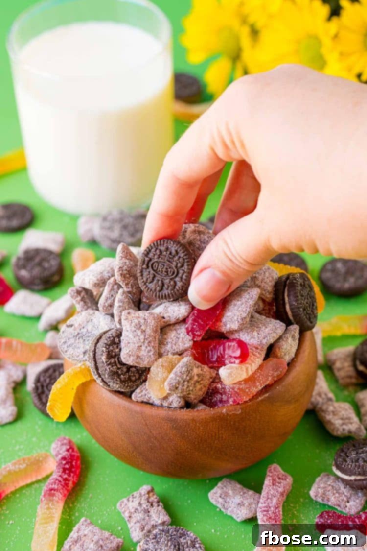 A womna's hand grabby some dirt cake muddy buddies from a wooden bowl.