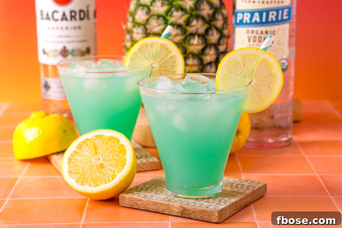 Mermaid's Paradise Elixir 4 Two glasses filled with vibrant blue Mermaid Punch, garnished with fresh fruit, sitting on a coaster.