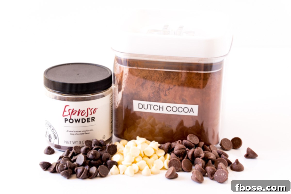 A selection of key ingredients laid out on a clean surface, ready to make triple chocolate chip cookies, including various chocolate chips, cocoa, and flour.