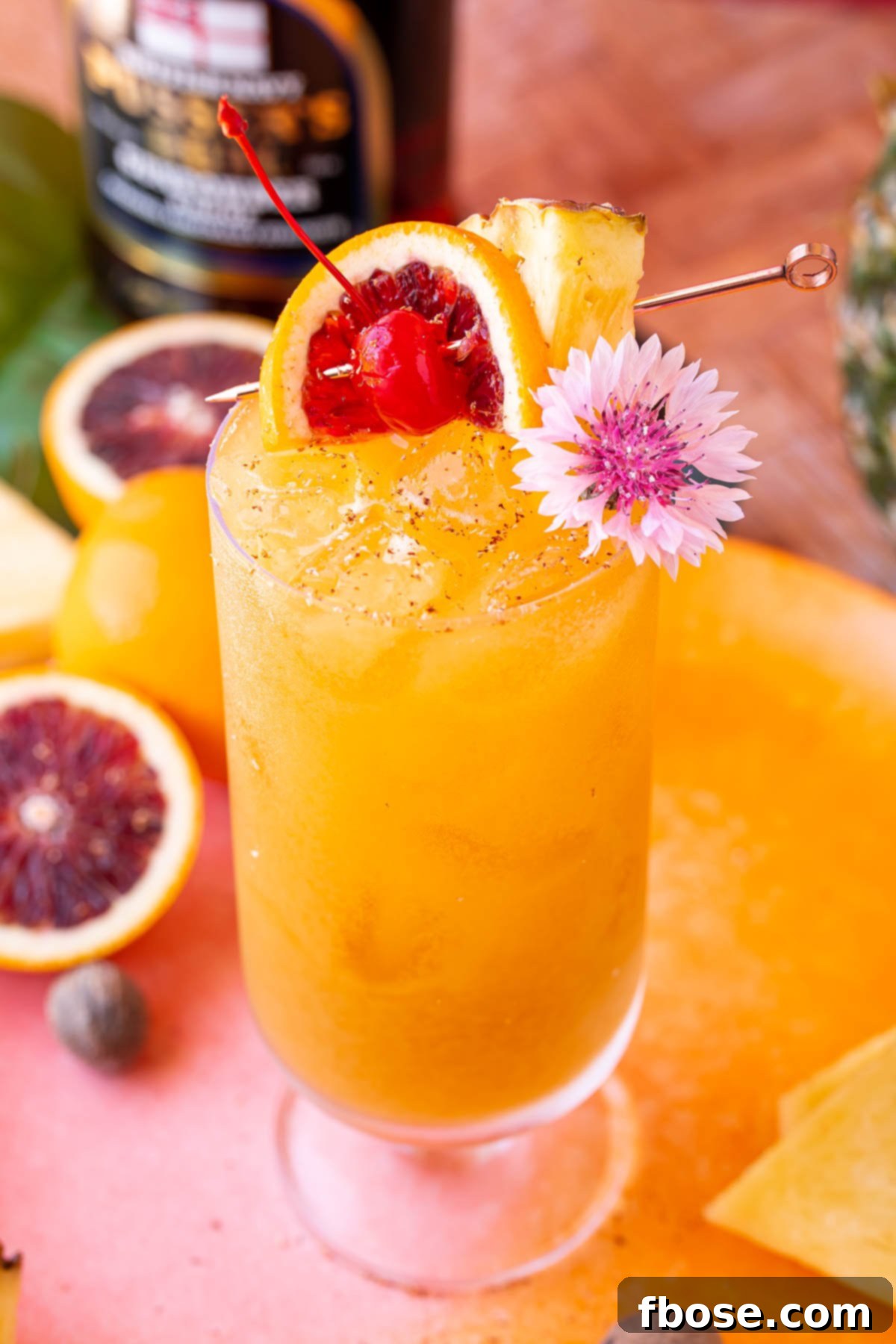 Vibrant Painkiller cocktail in an elegant stemmed highball glass, beautifully garnished with a fresh pineapple wedge, a bright orange slice, a cheerful maraschino cherry, and a tropical flower.