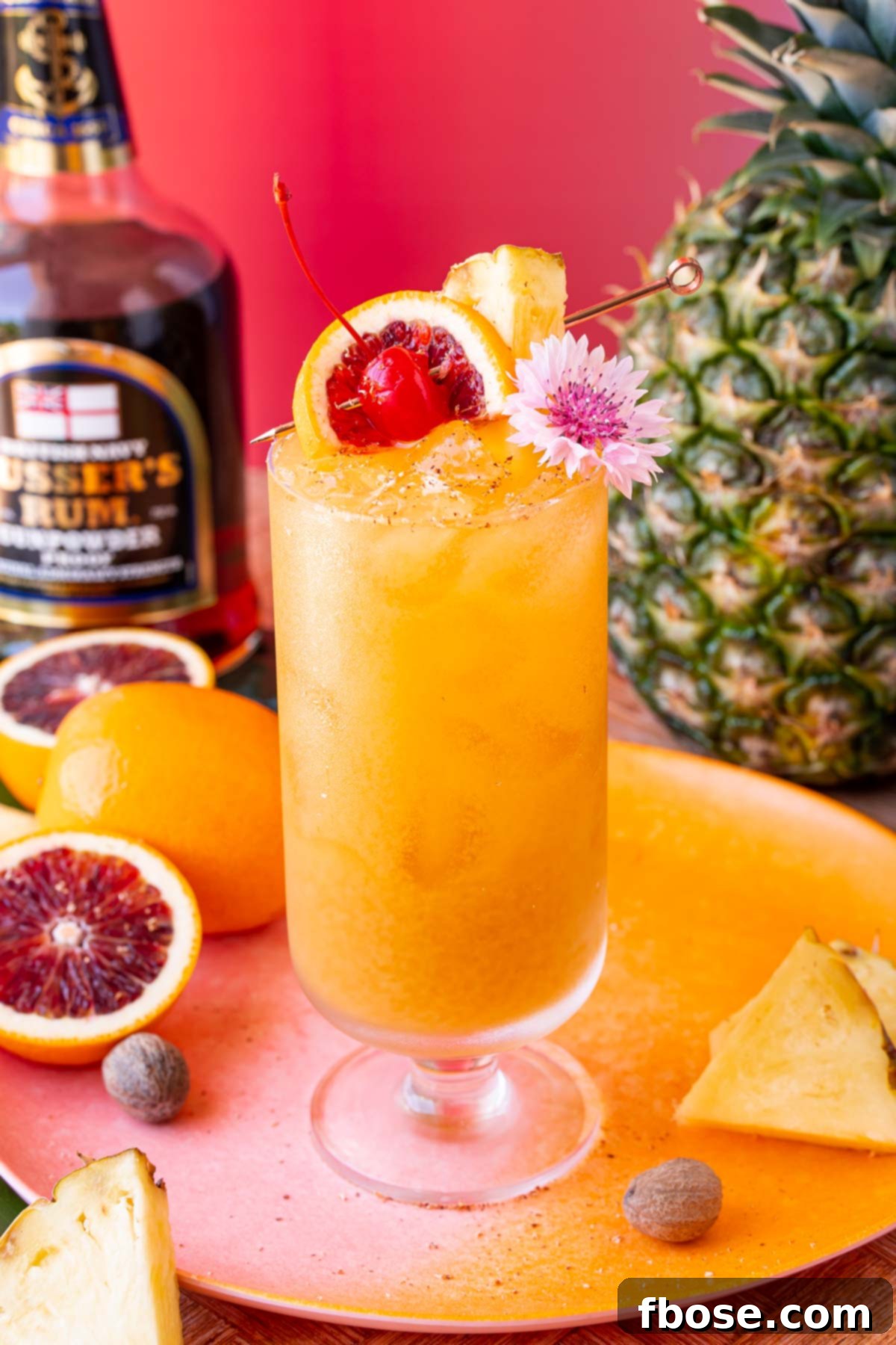 A beautifully presented Painkiller cocktail in a stemmed highball glass, artfully garnished with a fresh pineapple wedge, a vibrant orange slice, a classic maraschino cherry, and a delicate tropical flower.