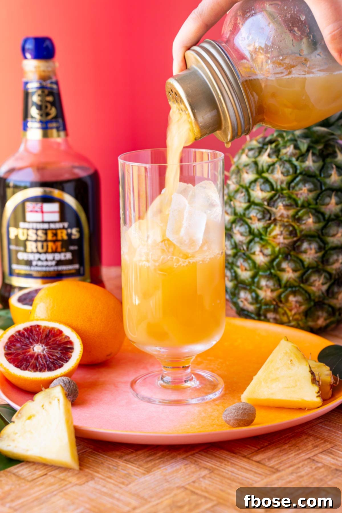 A skillful pour: a cocktail shaker expertly empties a painkiller drink into a highball glass filled with ice, creating a refreshing cascade.