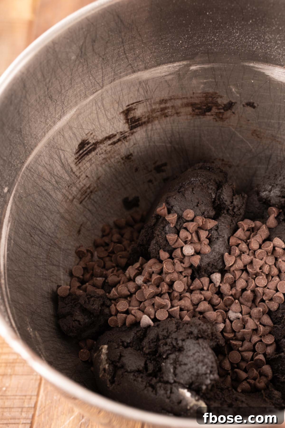 Chocolate chips being added to black cocoa cookie dough.