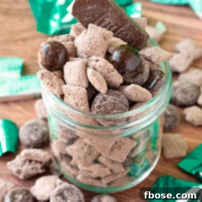 No-Bake Mint Chocolate Muddy Buddies 6 Mint chocolate muddy buddies in a jar on a wooden table surrounded my muddy buddies and mint candies.