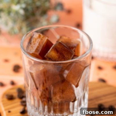 Coffee ice cubes in a glass with coffee beans scattered around it.