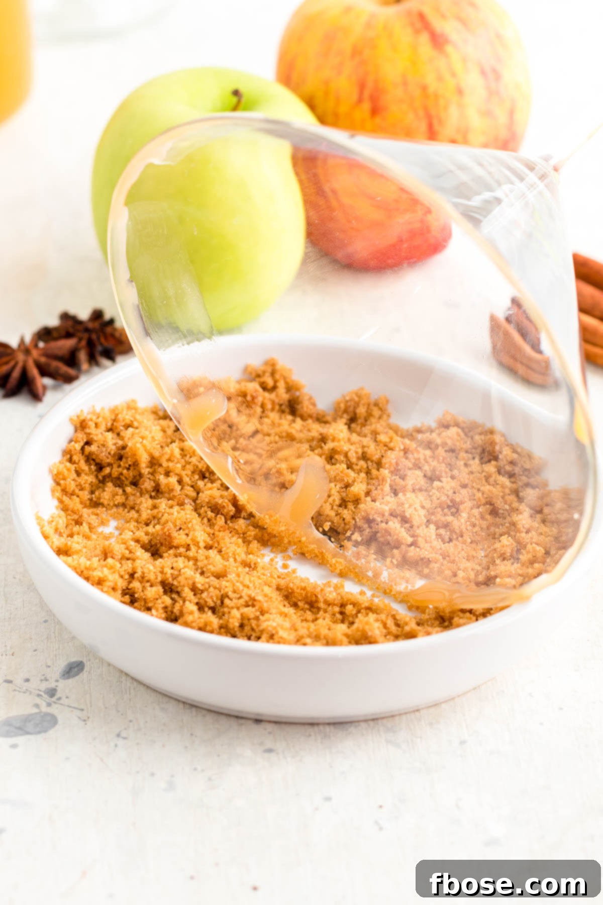 A close-up view of a martini glass, its rim being perfectly dipped in a mixture of brown sugar and cinnamon, preparing it for the delicious apple cider martini.