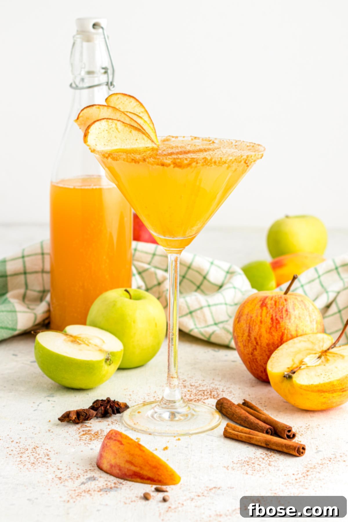 A sparkling martini glass filled with a perfectly mixed apple cider martini, artfully presented on a pristine white table.