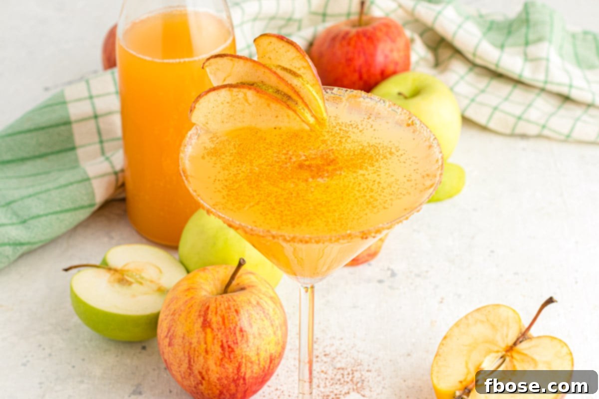 A close-up photograph of an apple cider martini presented on a white table, accompanied by a folded green napkin, emphasizing its inviting appearance.