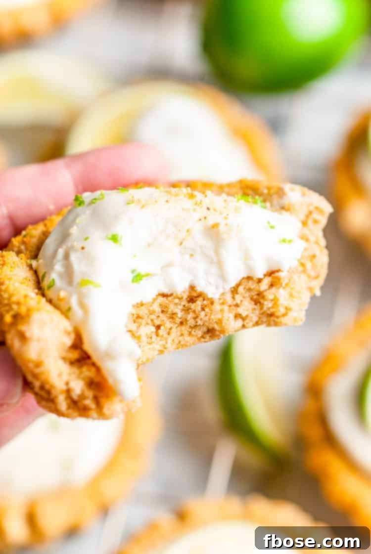 A woman's hand holding a Key Lime Pie Cookie with a bite taken out, showing the creamy green filling.