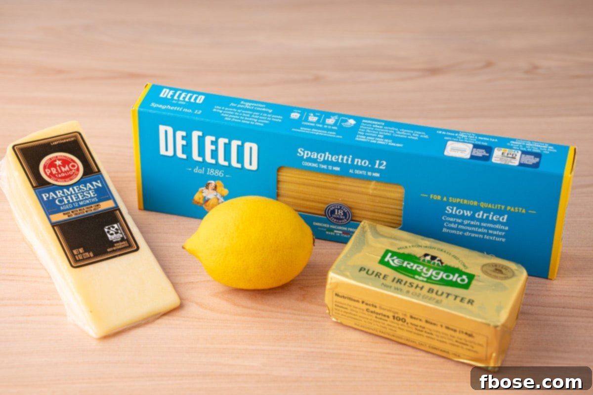 Ingredients to make spaghetti limone on a wooden table, including fresh lemons, a block of parmesan, and a bundle of spaghetti.