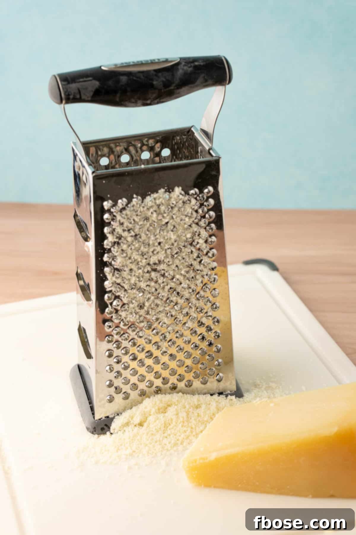 Parmesan cheese being grated into cheese dust using a box grater, demonstrating the technique.